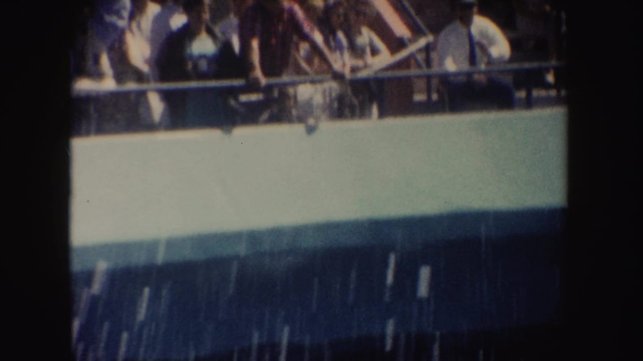 Spectators stand and sit behind a railing above a pool wall.