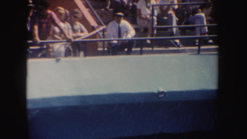 Spectators at a California marine performance look toward the pool from behind a railing in this 1962 8mm frame.