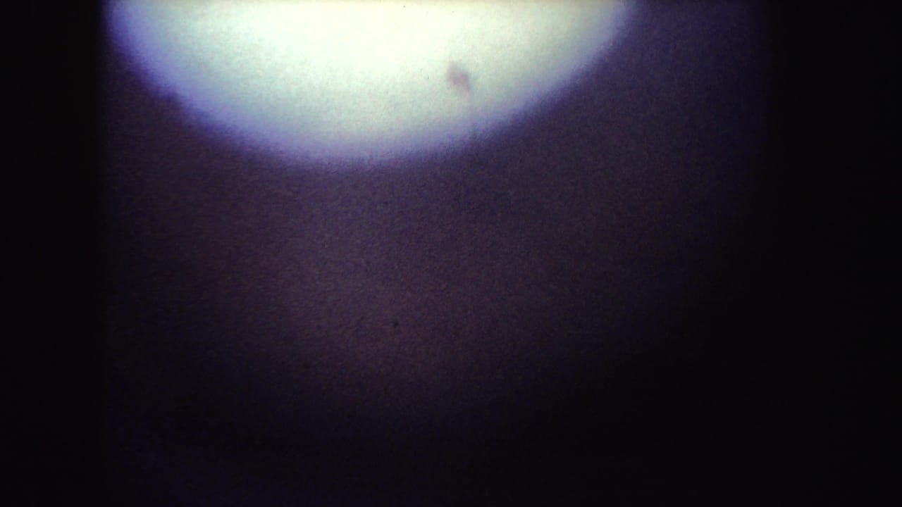 Dark, underexposed film frame with a bright circular flare near the top left.