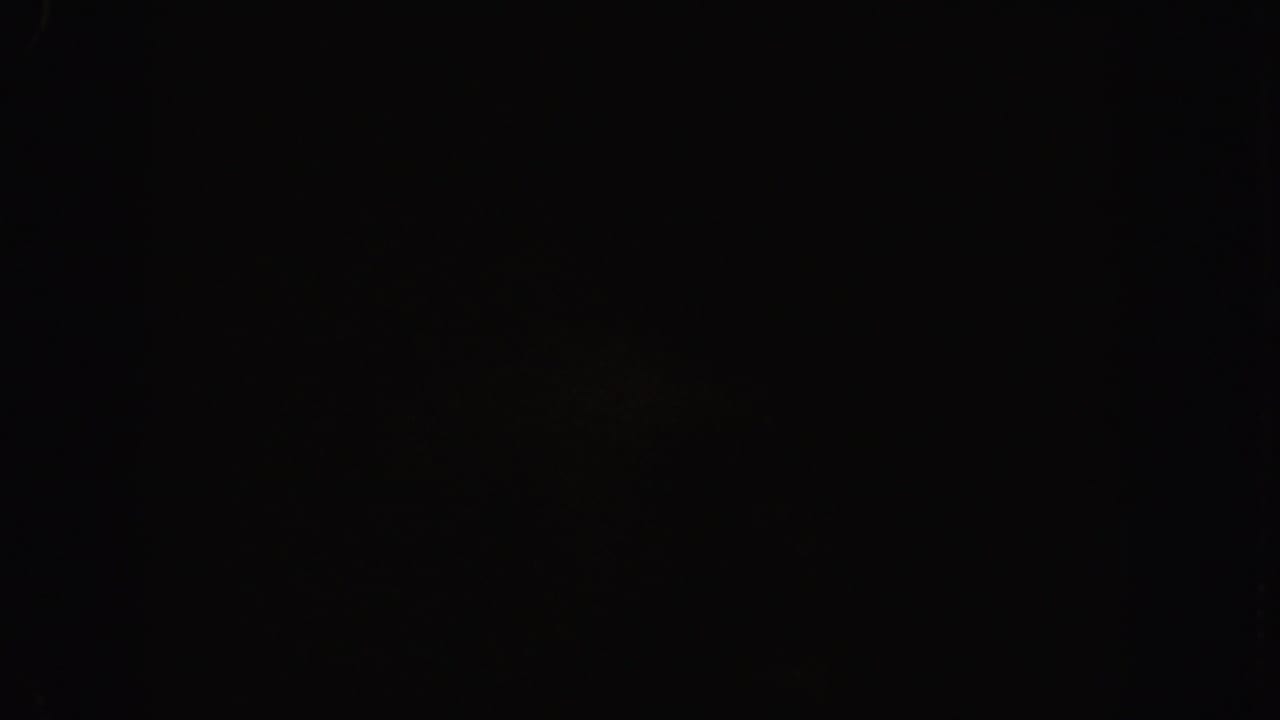 Nearly black frame with faint reddish-brown shapes and visible film grain.