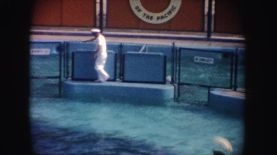 1962 California frame of a white-uniformed man walking along the pool edge with Marine World signage partly visible above.