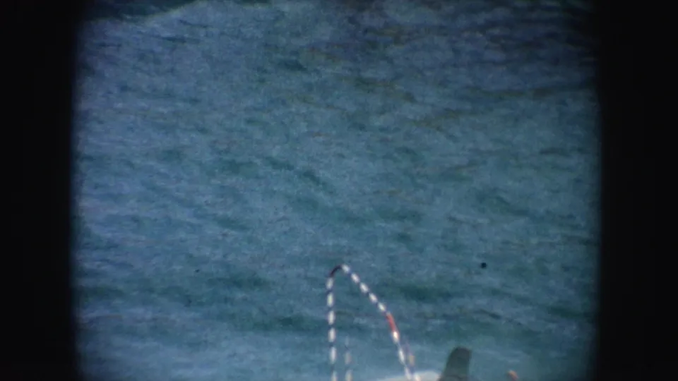 1962 California 8mm frame with a striped curved rail and part of a white platform visible near rippling blue-green water.