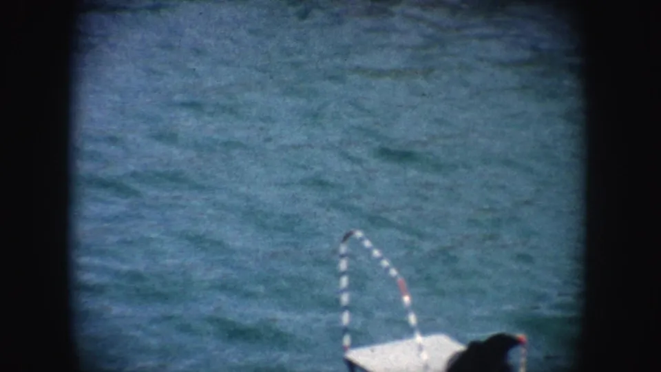 1962 California 8mm frame showing the corner of a white platform and striped curved rail against textured blue-green water.