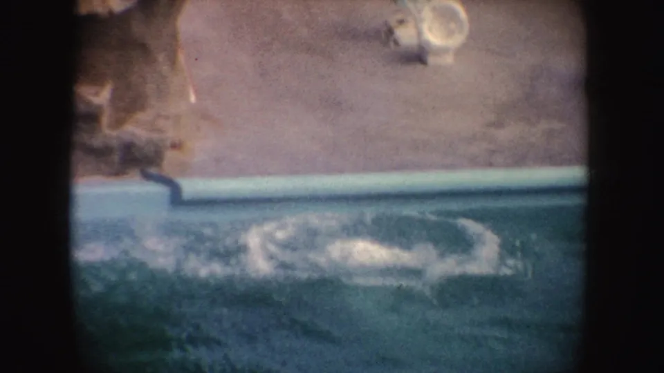 Blue-green pool water splashes after the seal dives into its zoo enclosure pool, captured on 8mm film in 1962.