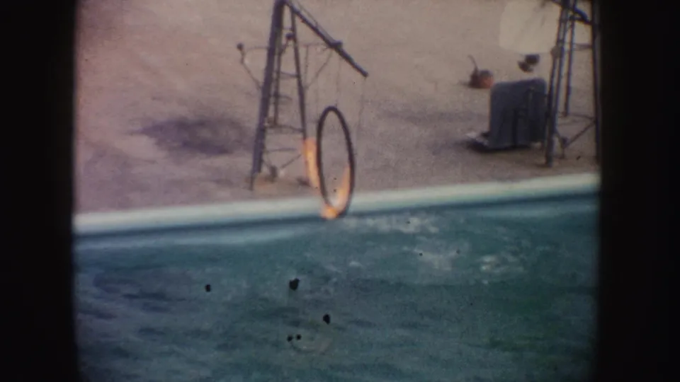 1962 California home-movie frame with a flaming hoop over a show pool and disturbed water from the marine animal stunt.