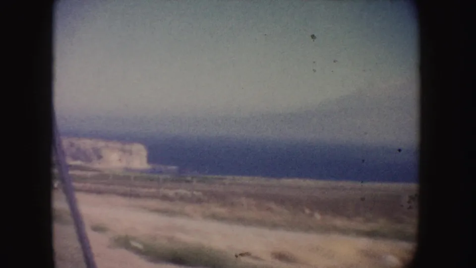 A brief California coastal view shows ocean, shoreline, and pale cliffs in soft, faded home-movie color.