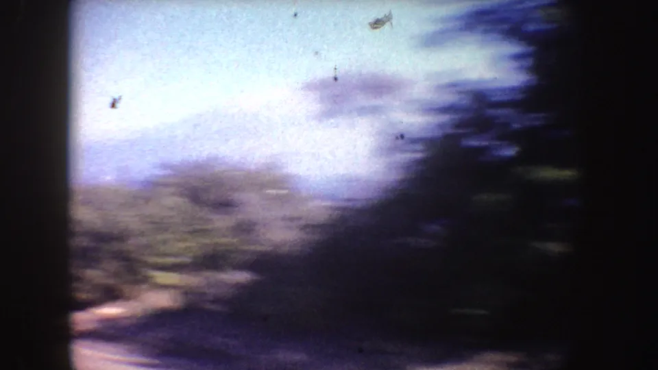 Motion-blurred 1962 California coastal frame showing roadside vegetation, bright sky, and blue ocean tones from a moving camera.
