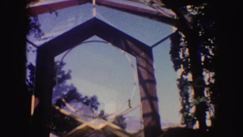 Final 8mm frame of the California outdoor chapel area, showing the geometric frame, stone altar, trees, and sky.