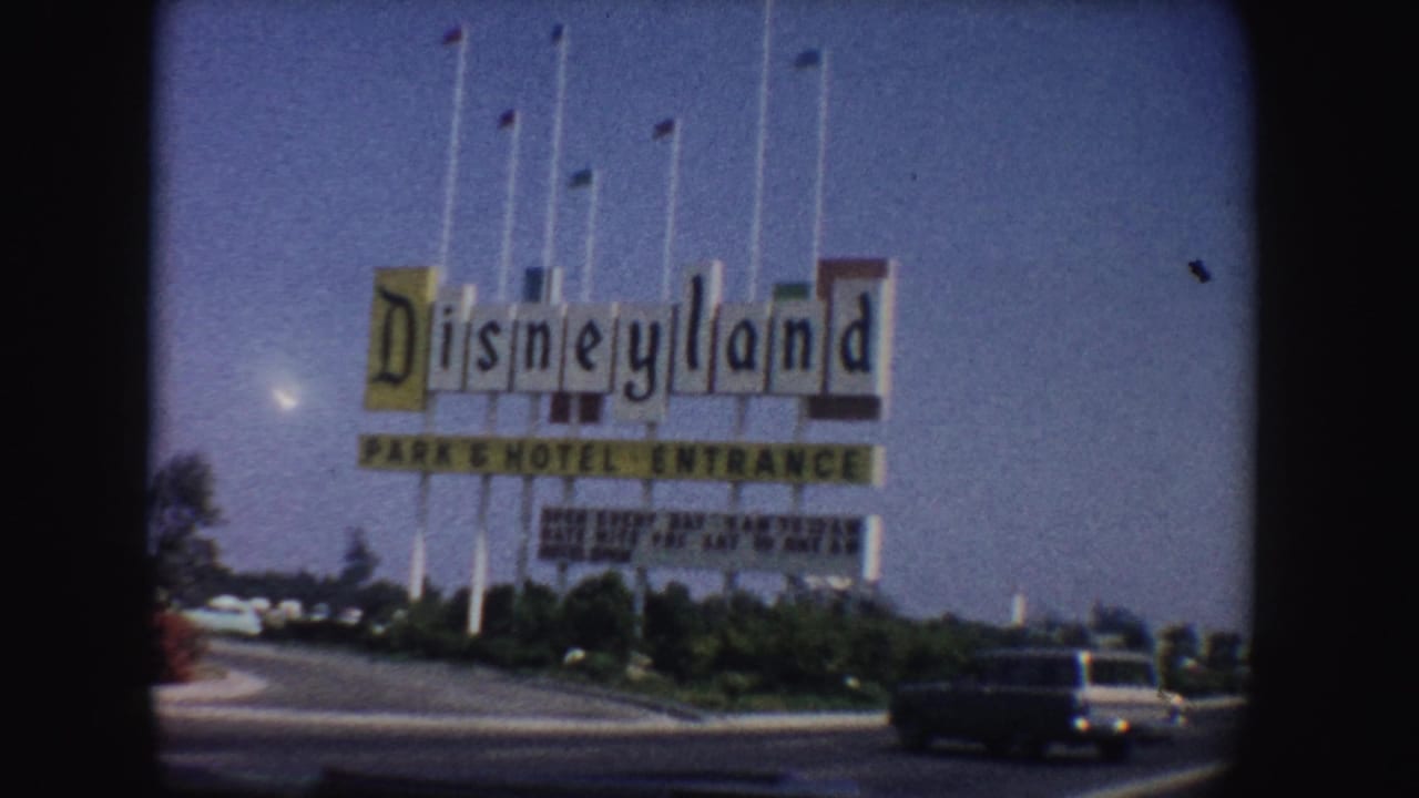 Disneyland entrance sign beside a road with a dark car in the foreground.