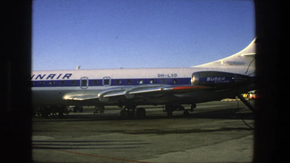 1975 8mm view of the Finnair aircraft midsection and tail area, with Super Constellation markings and airport pavement below.