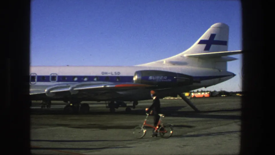1975 Stockholm airport view of a Finnair Super Caravelle, registration OH-LSO, with a suited man pushing a small bicycle across the tarmac.