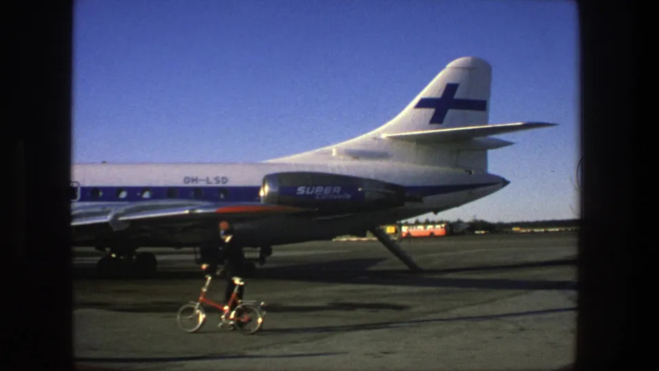 A suited man in a red cap pushes a small bicycle across the tarmac near the tail and rear fuselage of a Finnair Super Caravelle in Stockholm.