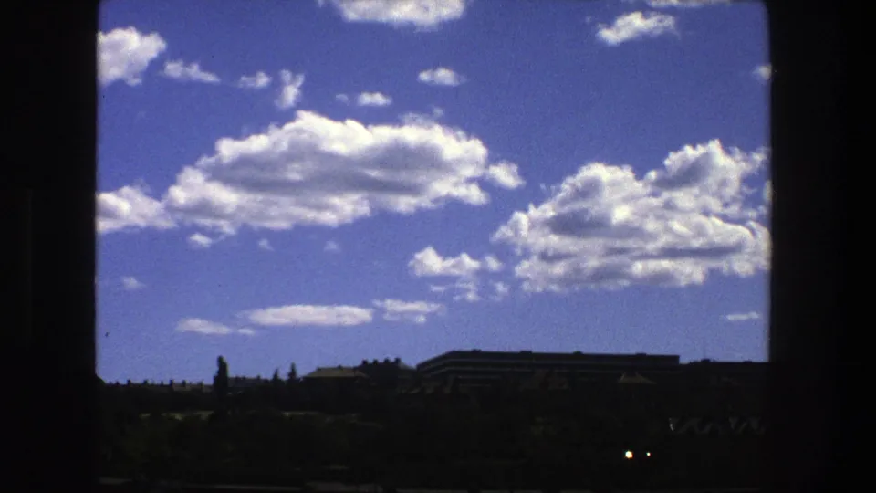 1975 Stockholm 8mm frame showing bright clouds over a low distant skyline, seen through dark window-like framing.