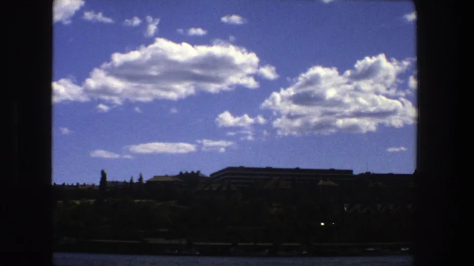 1975 Stockholm view of sunlit clouds and distant buildings, with a dark vertical frame splitting the composition.
