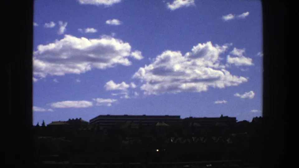 Late clip frame from 1975 Stockholm showing clouds, blue sky, low buildings, and dark structural framing.