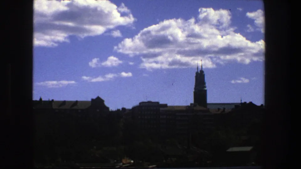 Stockholm skyline in 1975 with cumulus clouds, silhouetted buildings, trees, and a tower viewed through a dark window opening.