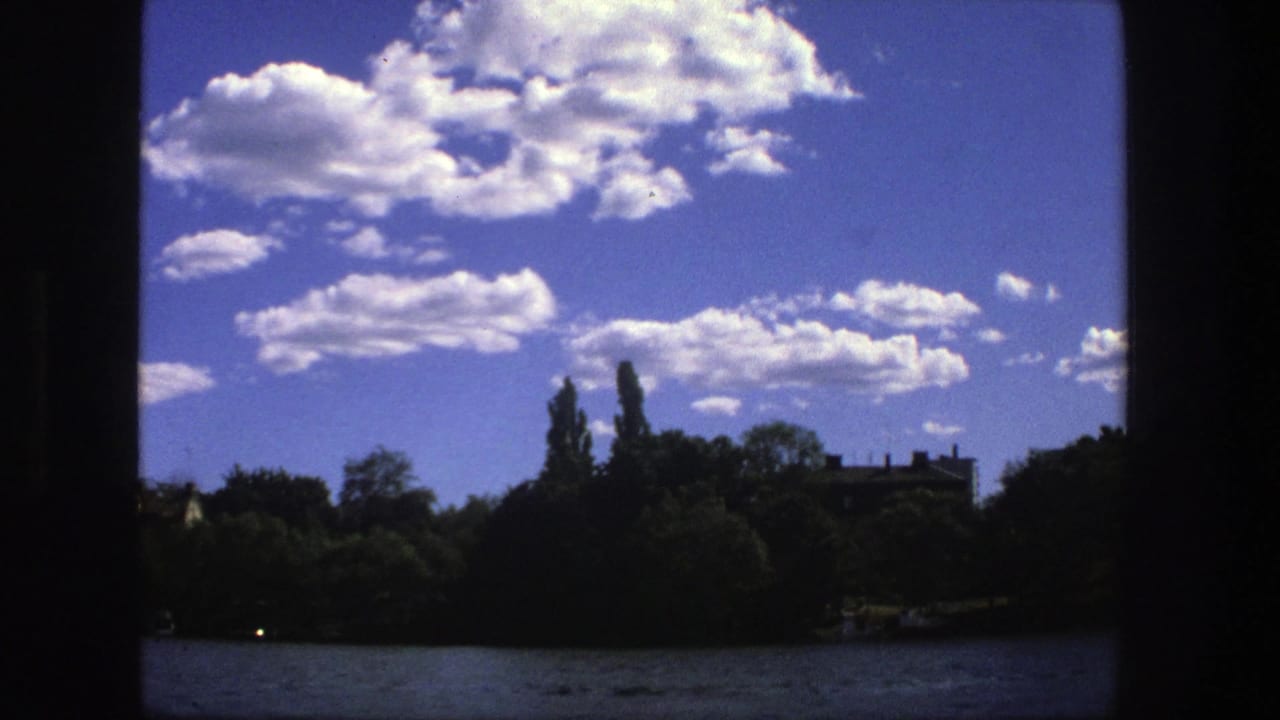 Treelined shore and water beneath a bright cloud-filled sky, with dark vertical framing.