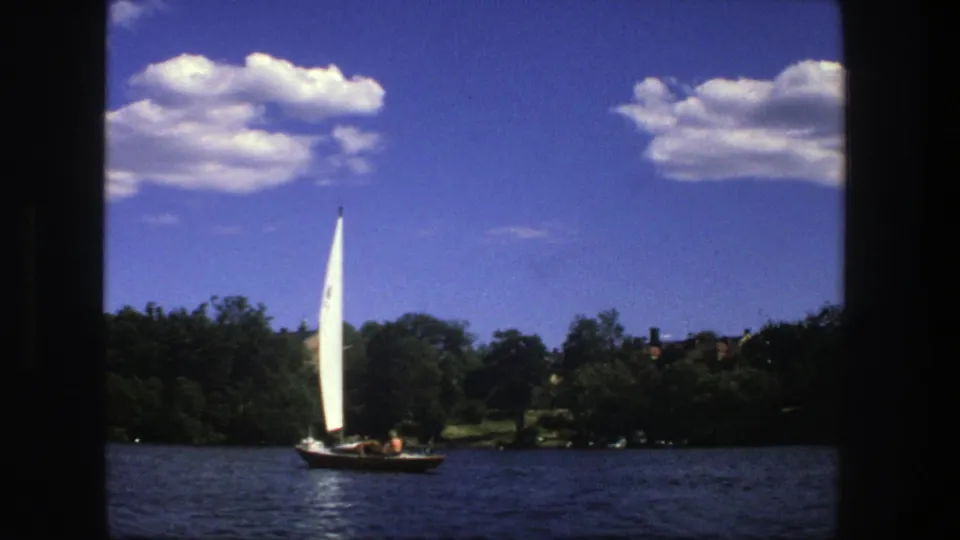 The final 1975 Stockholm frame holds on the sailboat against dark water, green banks, and bright summer clouds.