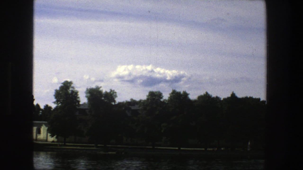 Similar waterfront view with trees, water, clouds, and dark vertical film borders.