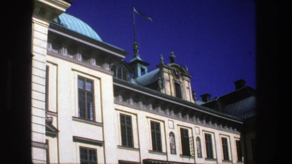 1975 Stockholm home-movie frame of a grand classical building exterior with green roof sections, decorative roofline, and tall windows.