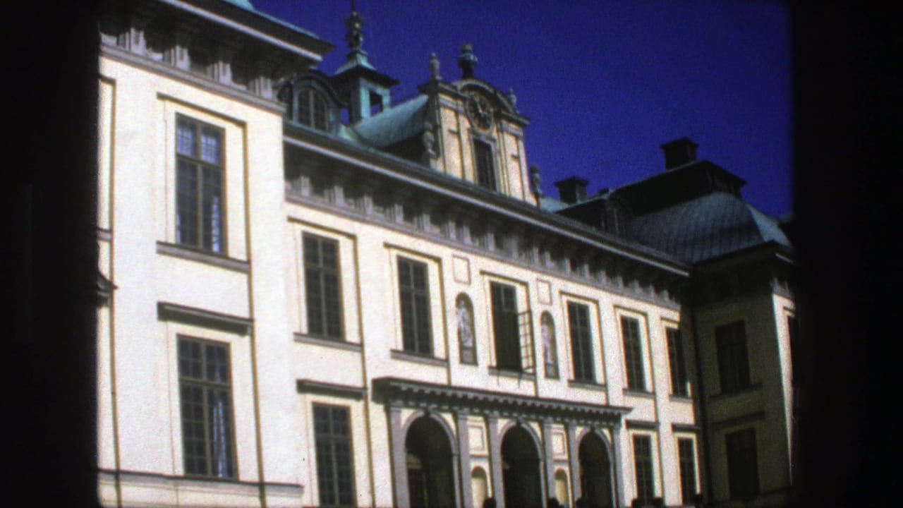 Pale historic building with arched entrance, tall windows, copper domes, and blue sky.