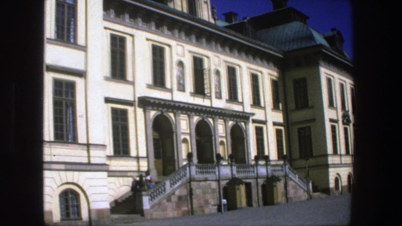 1975 Stockholm 8mm frame showing a classical building facade with tall windows, arched entries, broad stone stairs, and small background visitors.