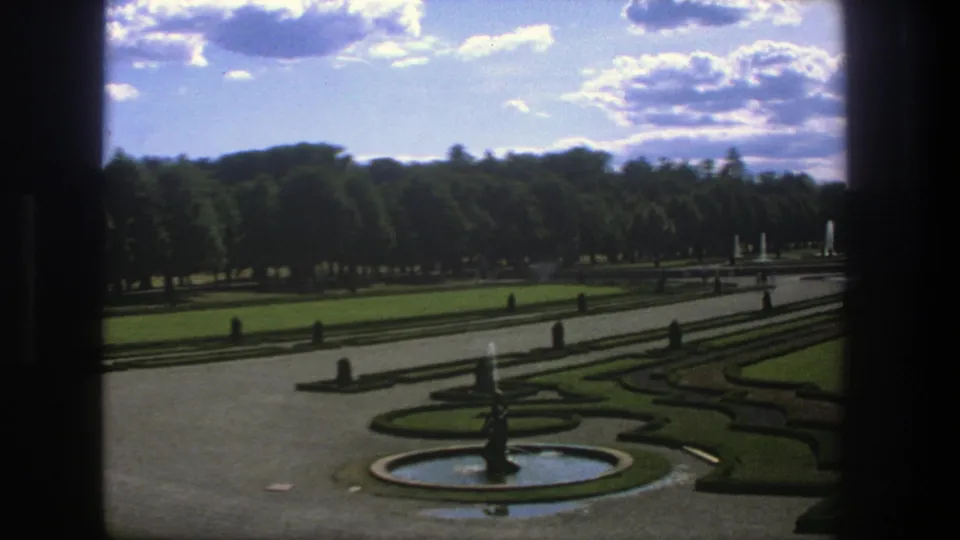 1975 Stockholm frame showing the formal garden from above, with a circular fountain, geometric planting beds, paved paths, and trees beyond.