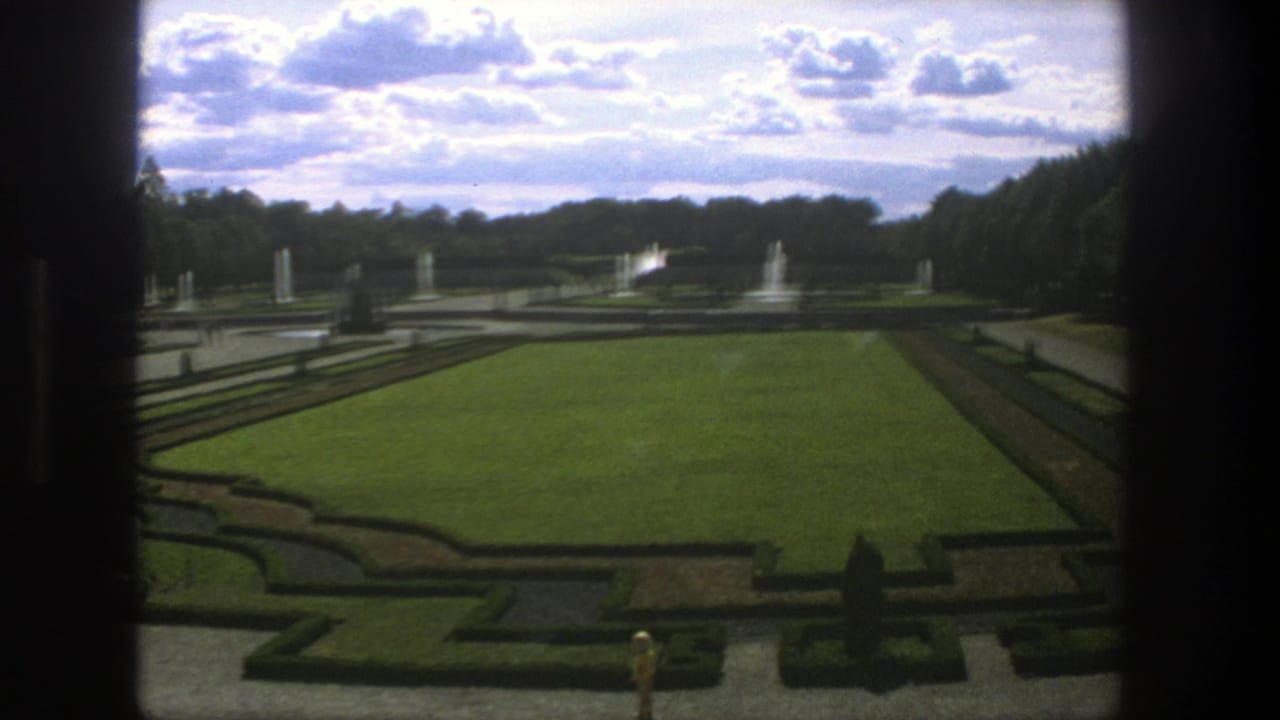 1975 Stockholm garden view showing a central lawn, clipped hedges, fountains, statues, tree rows, and dark window or frame edges.