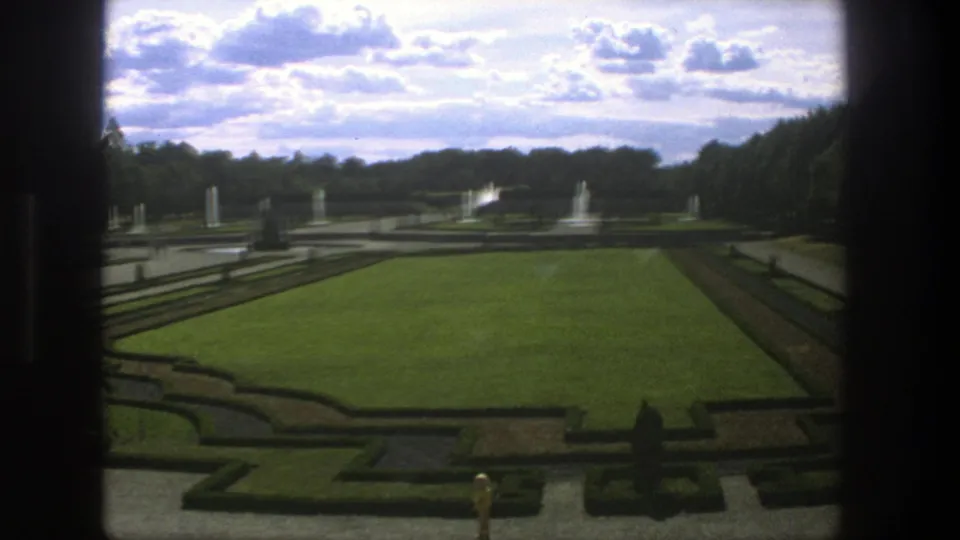 1975 Stockholm garden view showing a central lawn, clipped hedges, fountains, statues, tree rows, and dark window or frame edges.