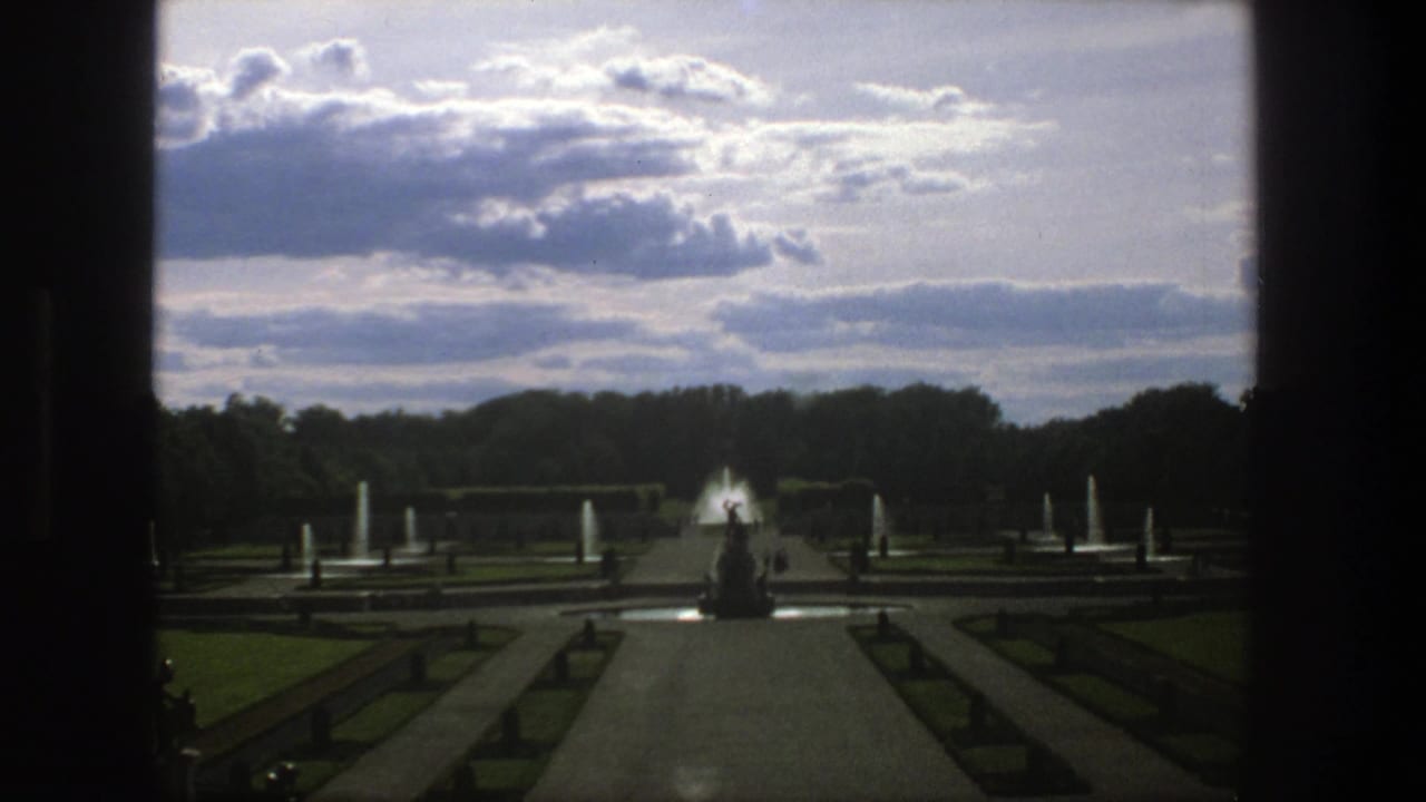 Central fountain garden view with lawns, paths, and cloudy sky.