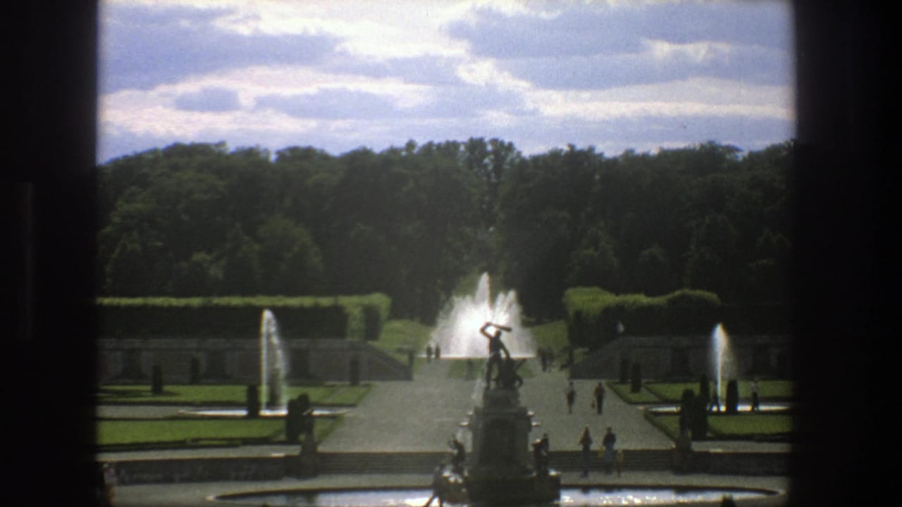 1975 Stockholm home-movie view of a formal garden with a central statue fountain, smaller water jets, hedges, and visitors on paths.