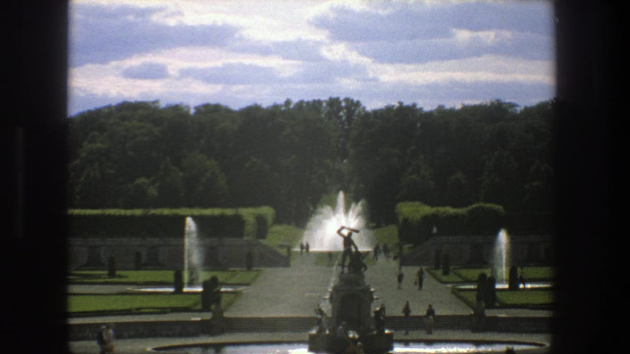 Symmetrical garden paths with a statue fountain, water jets, hedges, and small visitor figures.