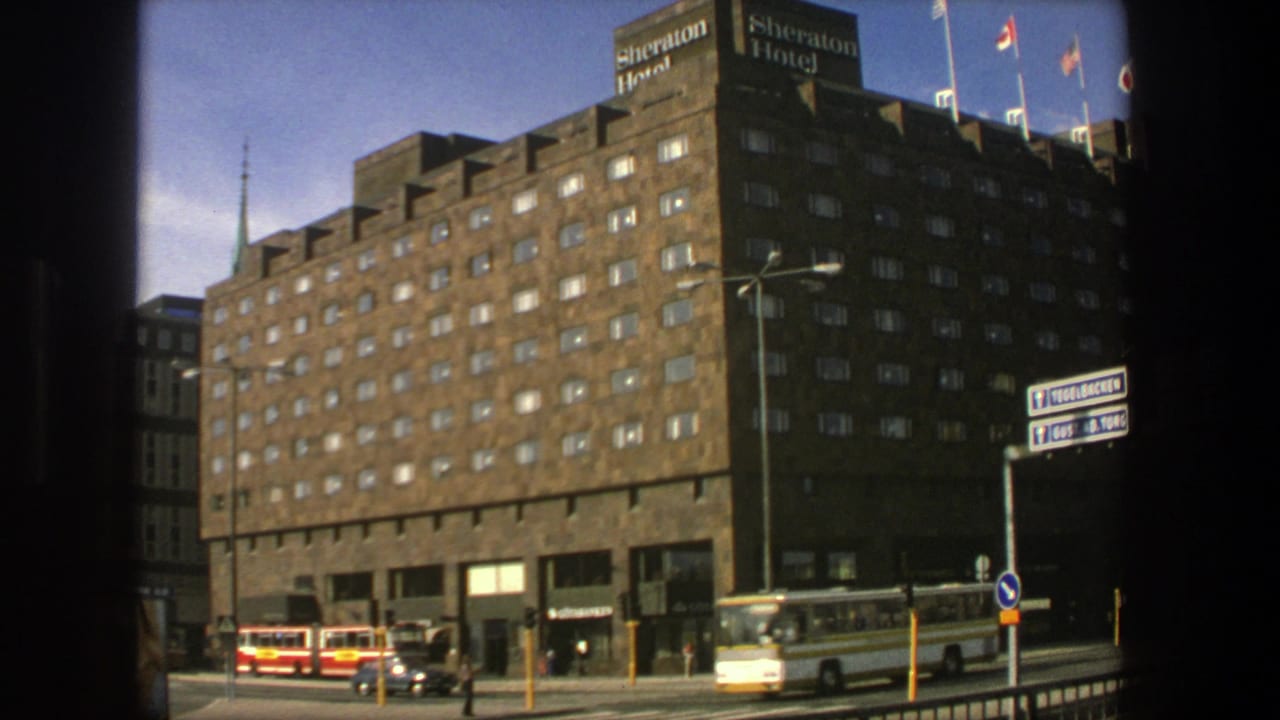 1975 Stockholm street view showing the Sheraton Hotel exterior, passing buses and cars, rooftop flags, and directional road signs.