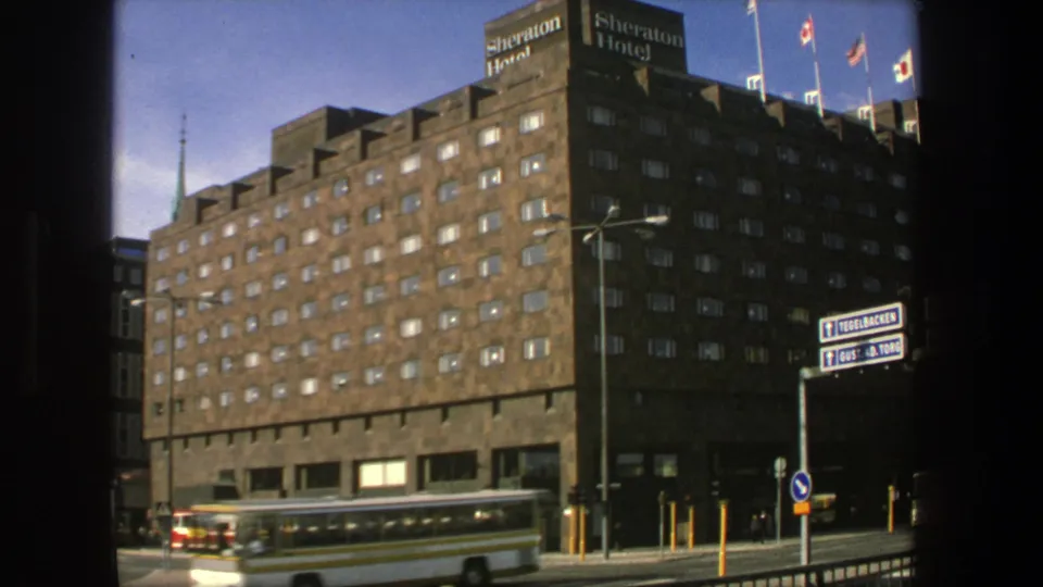Stockholm street scene from 1975 showing the Sheraton Hotel facade, a bus, cars, rooftop flags, and directional signs.