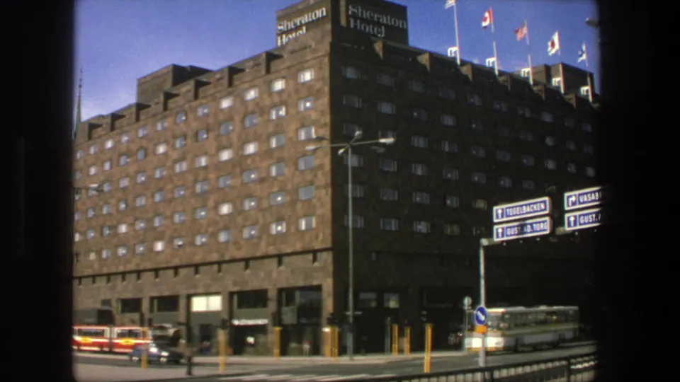 1975 Stockholm street view of the Sheraton Hotel corner with flags above, traffic below, and directional signs in the foreground.