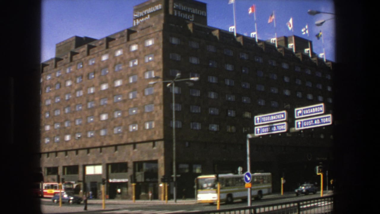 Sheraton Hotel exterior with flags, street signs, a bus, cars, and pedestrians.