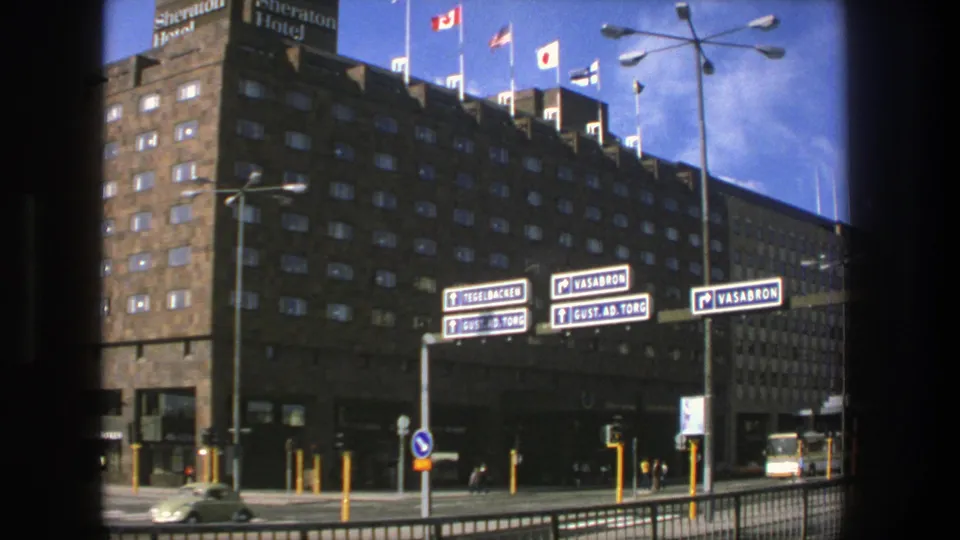 1975 Stockholm view of the Sheraton Hotel corner with flags above, Vasabron signs, cars, and small pedestrians at street level.