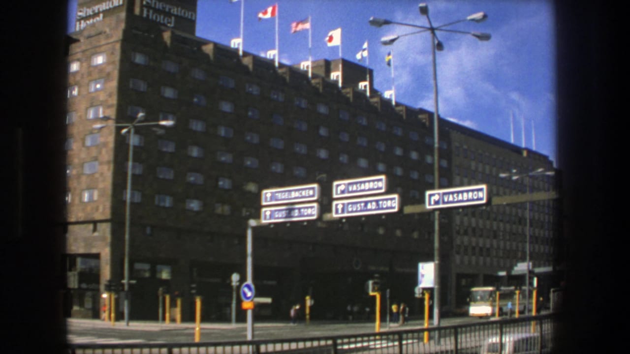 Sheraton Hotel facade with rooftop flags, street signs, traffic lights, and a bus at the curb.