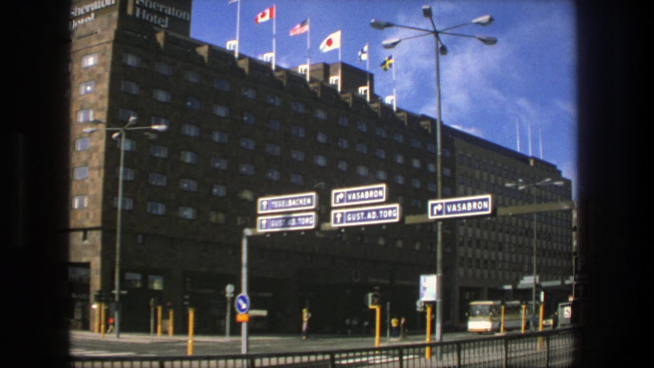 1975 Stockholm view of the Sheraton Hotel and nearby road signs for Vasabron and Gust. Ad. Torg, with flags, poles, and street traffic.
