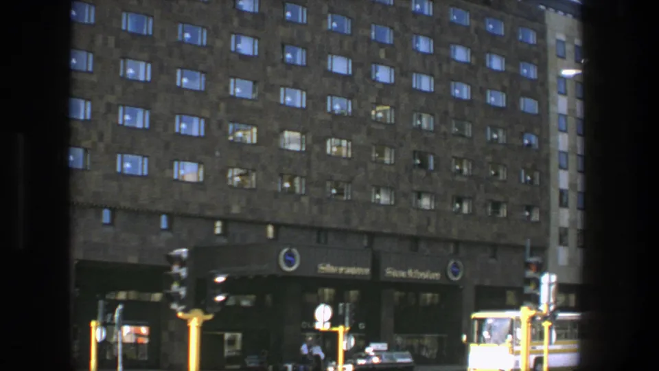 1975 Stockholm street-level view of the Sheraton facade and entrance area, with cars, a yellow-white bus, traffic lights, and small pedestrians.