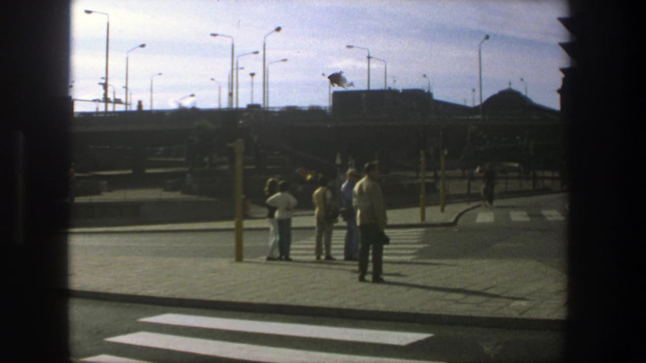 Pedestrians wait near a zebra crossing, seen through a dark window frame.