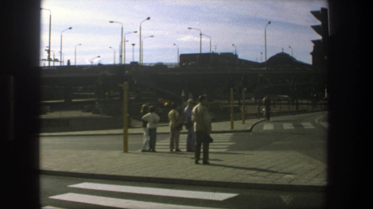 Small group stands at a curb by a crosswalk under tall streetlights.