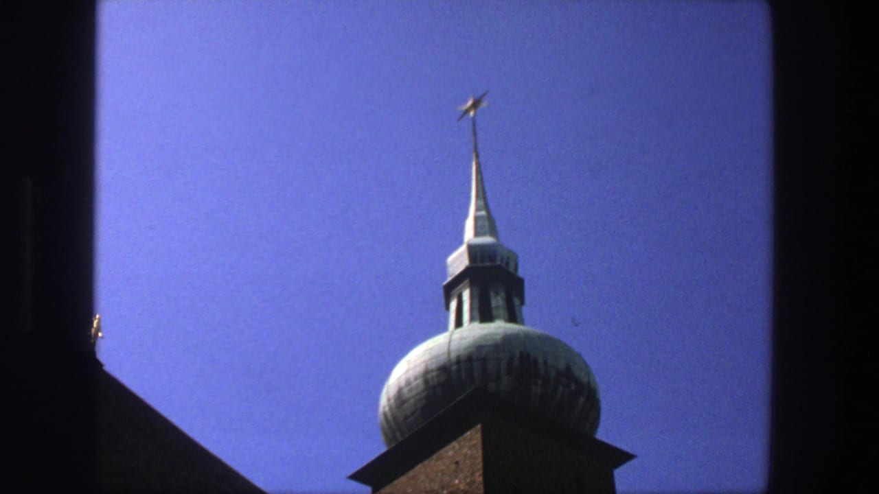 1975 Stockholm 8mm frame showing a brown brick church tower with a pale domed cupola and star finial against blue sky.