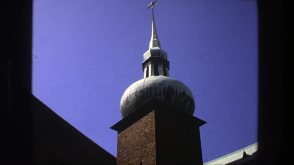 1975 Stockholm 8mm frame showing the church tower more fully, with dark framing edges and a blue sky backdrop.