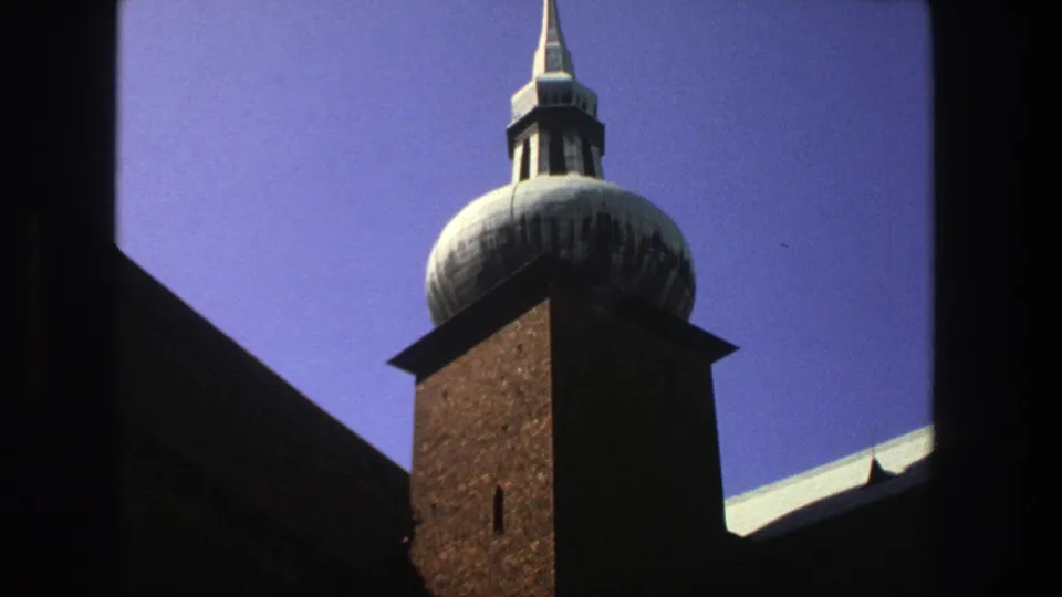 1975 Stockholm 8mm frame of a brown brick church tower and pale domed cupola, with a roof edge visible at lower right.