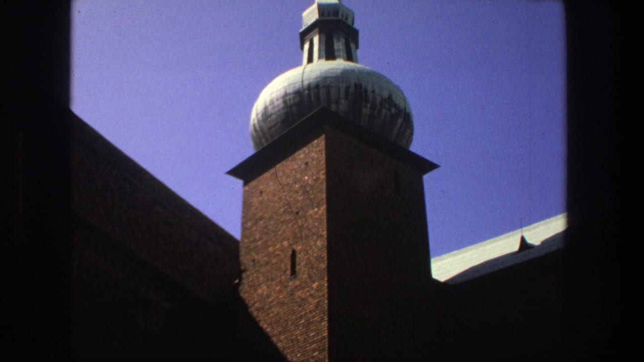 1975 Stockholm 8mm view of a brick religious building tower with a domed spire against blue sky, partly framed by dark foreground edges.