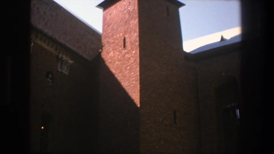 A 1975 8mm frame shows the Stockholm brick religious building from below, with sunlit masonry, deep shadow, a tower, and arched openings.