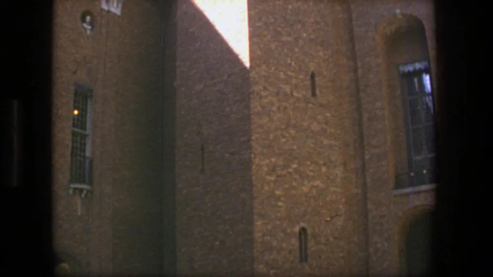The pan reveals more of the Stockholm brick religious building, including sunlit wall surfaces, narrow windows, and the edge of the tower.