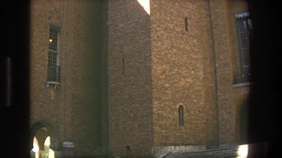 1975 Stockholm 8mm frame showing a brown brick building facade with barred windows, an arched passage, and strong sunlight across the masonry.