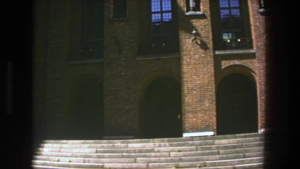1975 Stockholm 8mm view of a brick facade with arched openings, metal-grilled windows, and a wide stone staircase, partly obscured by film gate marks.